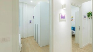 A corridor with a wardrobe, a bed with a blue pillow, and a wall-mounted light fixture. - Contessa Elegance Inn Vacation Rental, Rome (Roma)