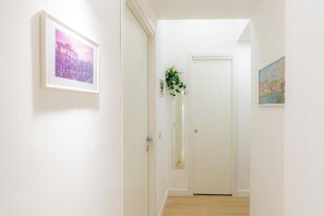 Ein Flur mit einem gerahmten Bild links, einer Tür am Ende und einer Pflanze in der Mitte.