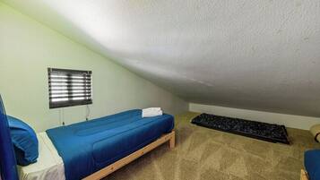 A small, single-bed room with a sloped ceiling, a window with blinds, and a carpeted floor.