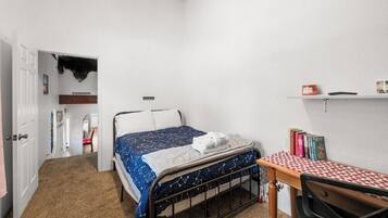 A bedroom with a bed, a desk, and a shelf with books.