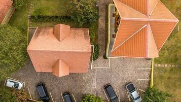 Vista aérea de un edificio con un diseño geométrico singular en su tejado, rodeado de un estacionamiento con varios coches.