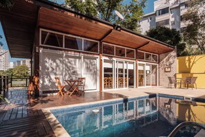 A modern building with a pool, wooden deck, and outdoor seating area.
