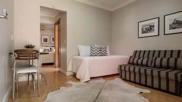Un dormitorio con una cama, un sofá a rayas, una silla, una alfombra y dos cuadros enmarcados en la pared.