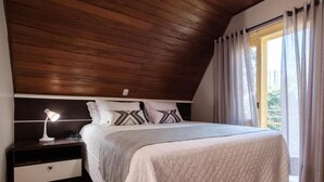 Ein Schlafzimmer mit Holzboden, einem Bett mit gesteppter Decke, einem Nachttisch mit Lampe und einem Fenster mit Vorhängen.