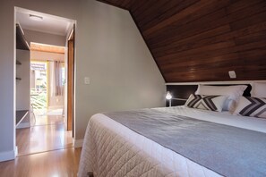 Un dormitorio con techo inclinado, una cama con cubrecama acolchado y una lámpara de noche.