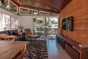 Un interior moderno con techo de madera, un sofá, una silla, una mesa de comedor y un televisor montado en la pared.