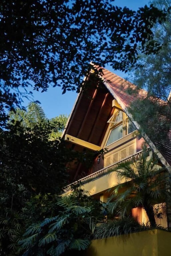 A building with a sloped roof, surrounded by dense foliage and a body of water.