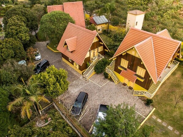 A cluster of wooden cabins with red roofs, surrounded by greenery, and a paved driveway with parked cars. - Pousada do Chalé (Bento Gonçalves)