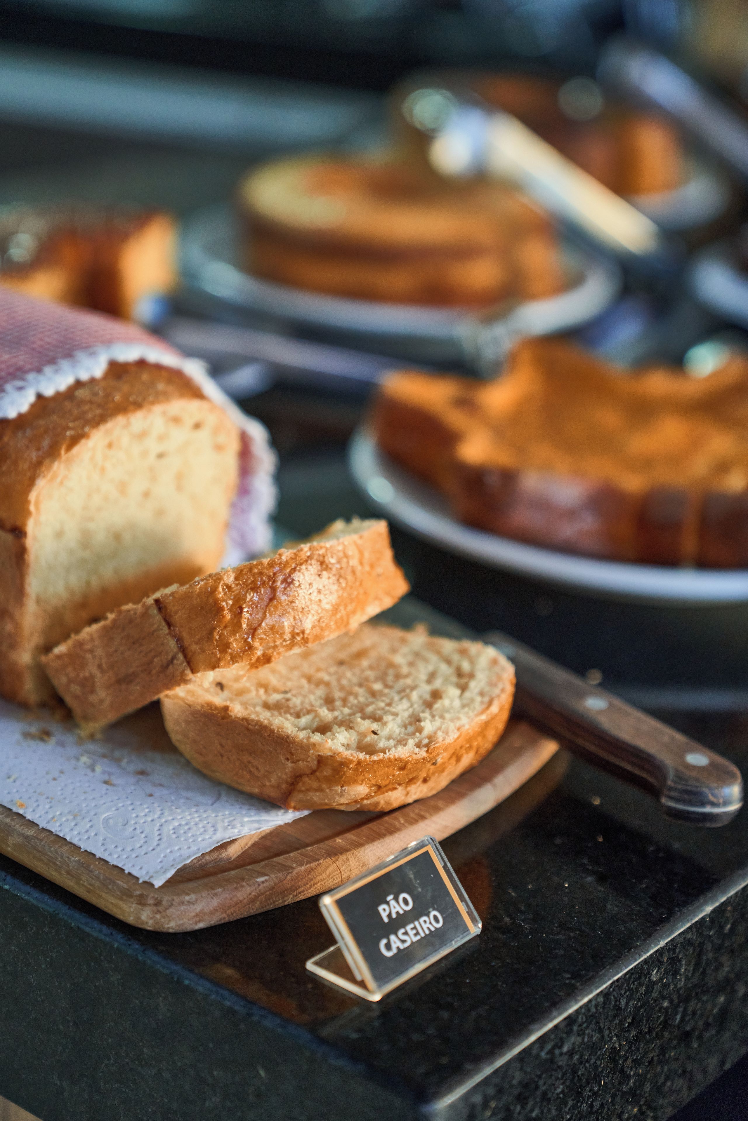 A display of various bread types on a wooden board with a label 'PAO CASERO'.