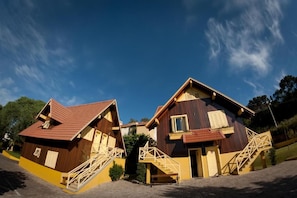 Two wooden houses with red roofs and yellow accents, connected by a staircase.