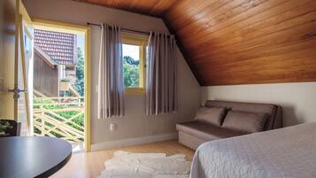 A bedroom with a wooden ceiling, a sofa, a bed, and a view of a garden through a window.