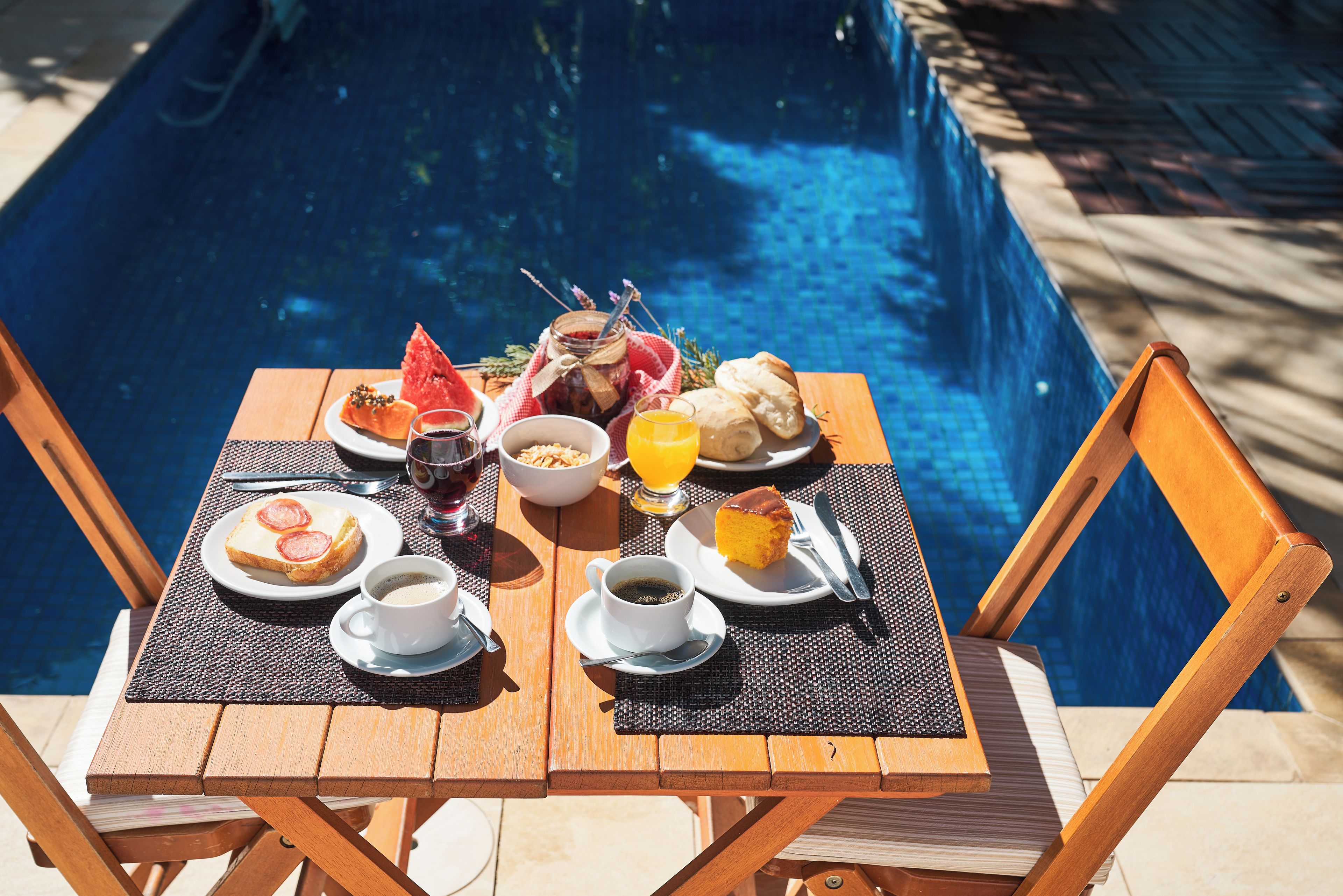 Ein Esstisch mit Frühstücksangeboten, einem Glas Saft und Blick auf einen Swimmingpool.