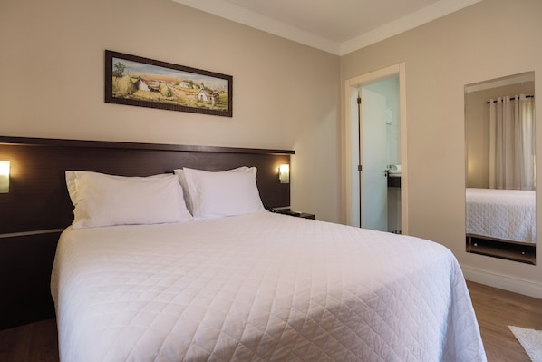 A hotel room with a large bed, a nightstand, a painting on the wall, and a mirror reflecting the bed.