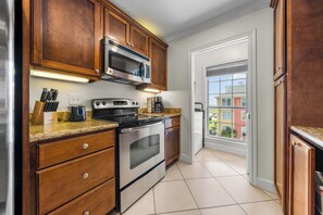 A kitchen with wooden cabinets, stainless steel appliances, a granite countertop, and a view through the door. - Salt & Summer at the Dawn condos with Ocean and Pool Views!  Family friendly! (Galveston)