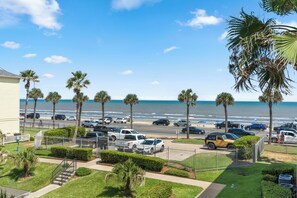 A parking lot with several cars, a beach in the background, and palm trees. - Salt & Summer at the Dawn condos with Ocean and Pool Views!  Family friendly! (Galveston)