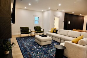 Ein modernes Wohnzimmer mit einer Eckcouch, zwei Sesseln, einem Couchtisch und einem gemusterten Teppich.
