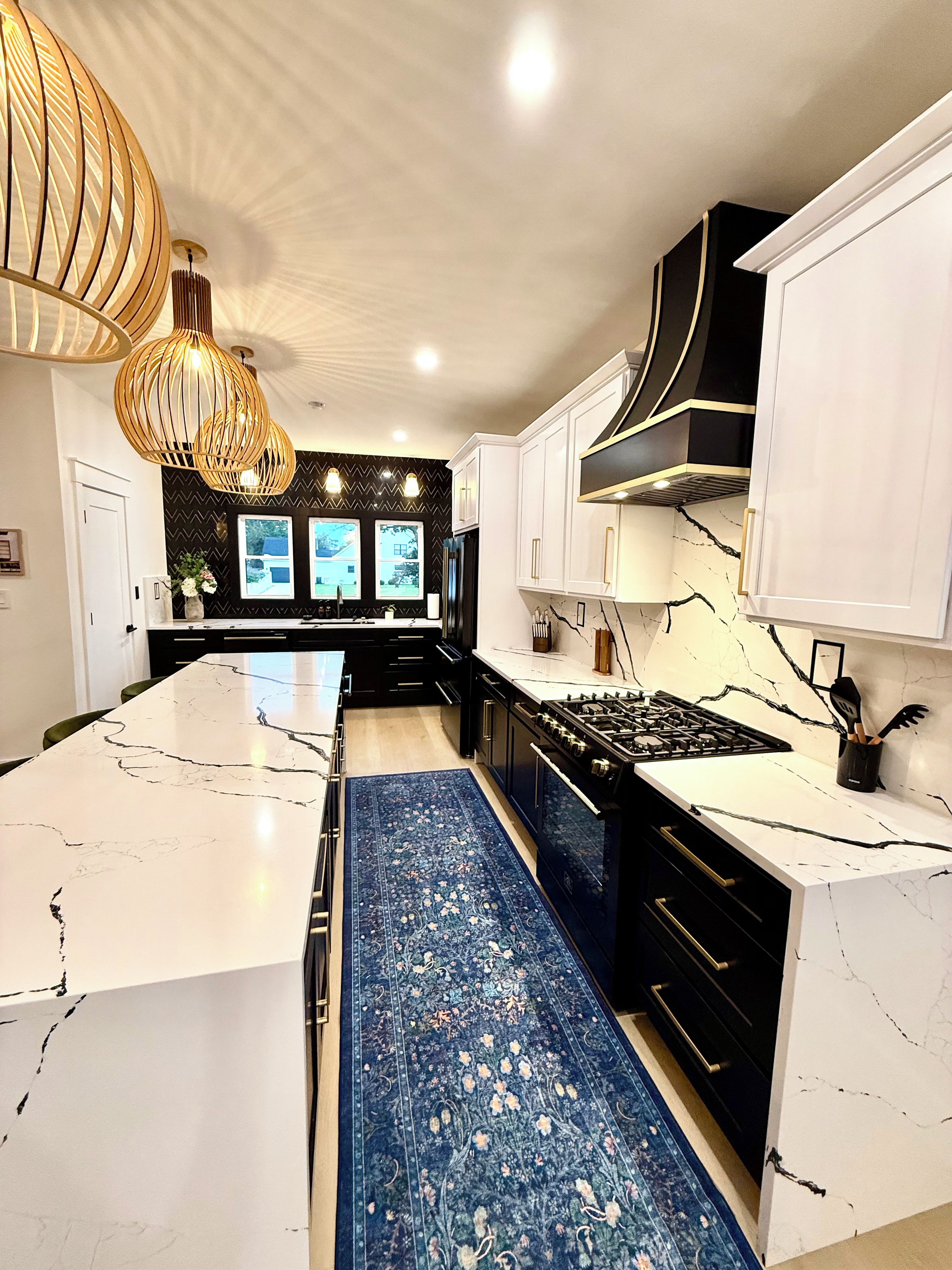 A modern kitchen with white marble countertops, a central island, black cabinetry, and a blue patterned rug.