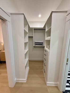 Ein begehbarer Kleiderschrank mit weißen Regalen, einem kleinen Fenster und einer eingebauten Heizung.