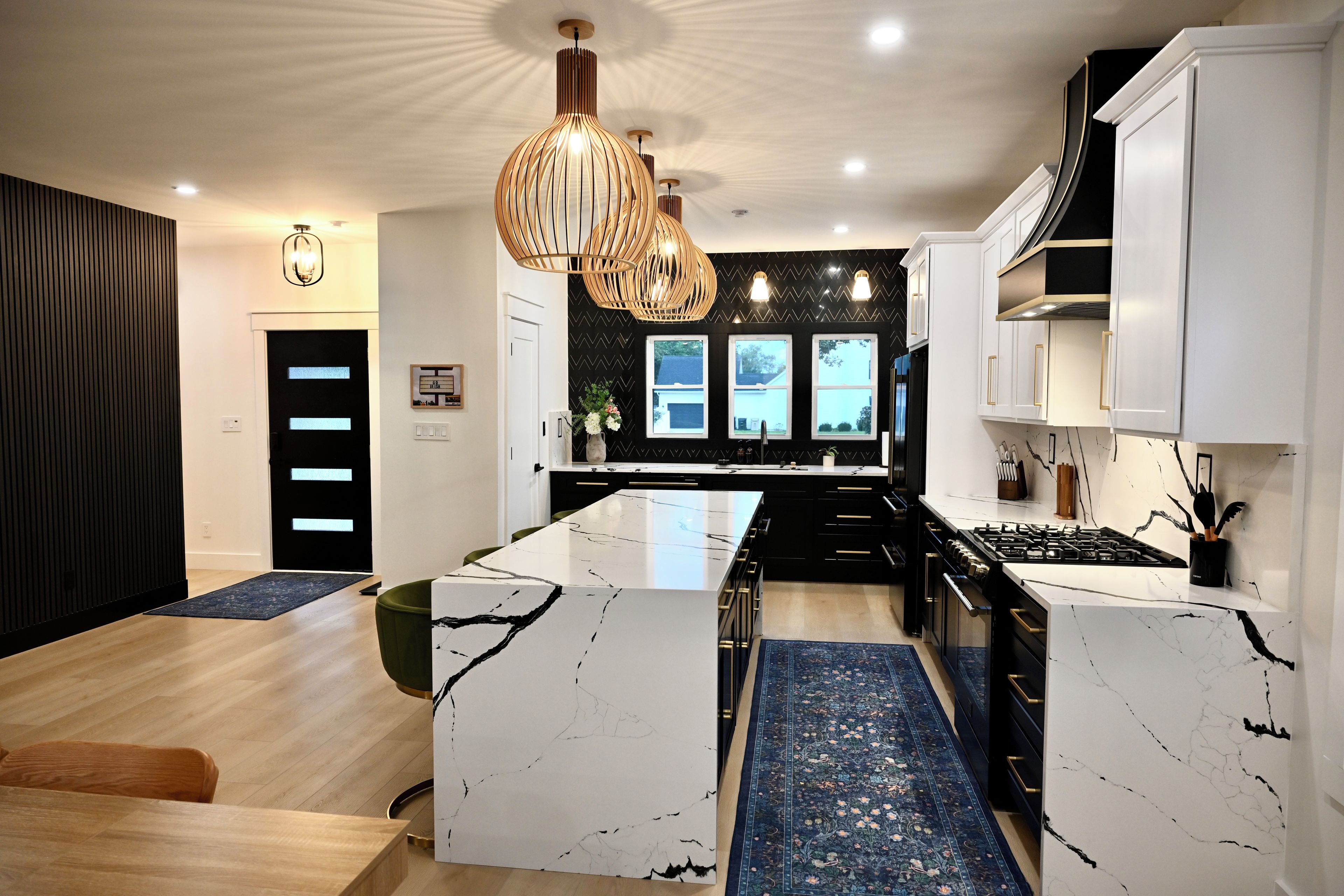 Een moderne keuken met een centraal eiland, zwarte kastjes en een kamerbreed tapijt met dessin.