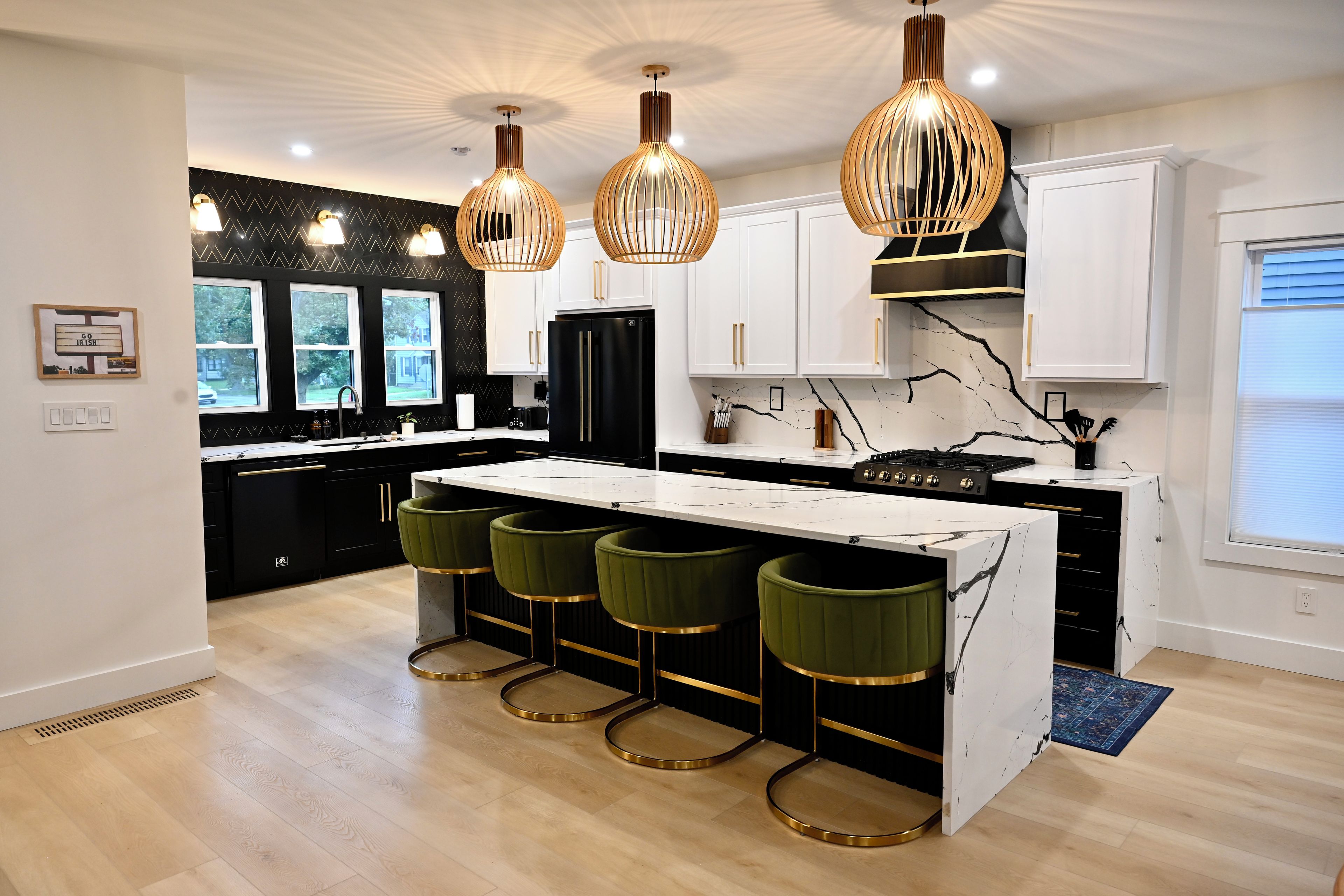 A modern kitchen with a central island, bar stools, pendant lighting, and a view of the outdoors.