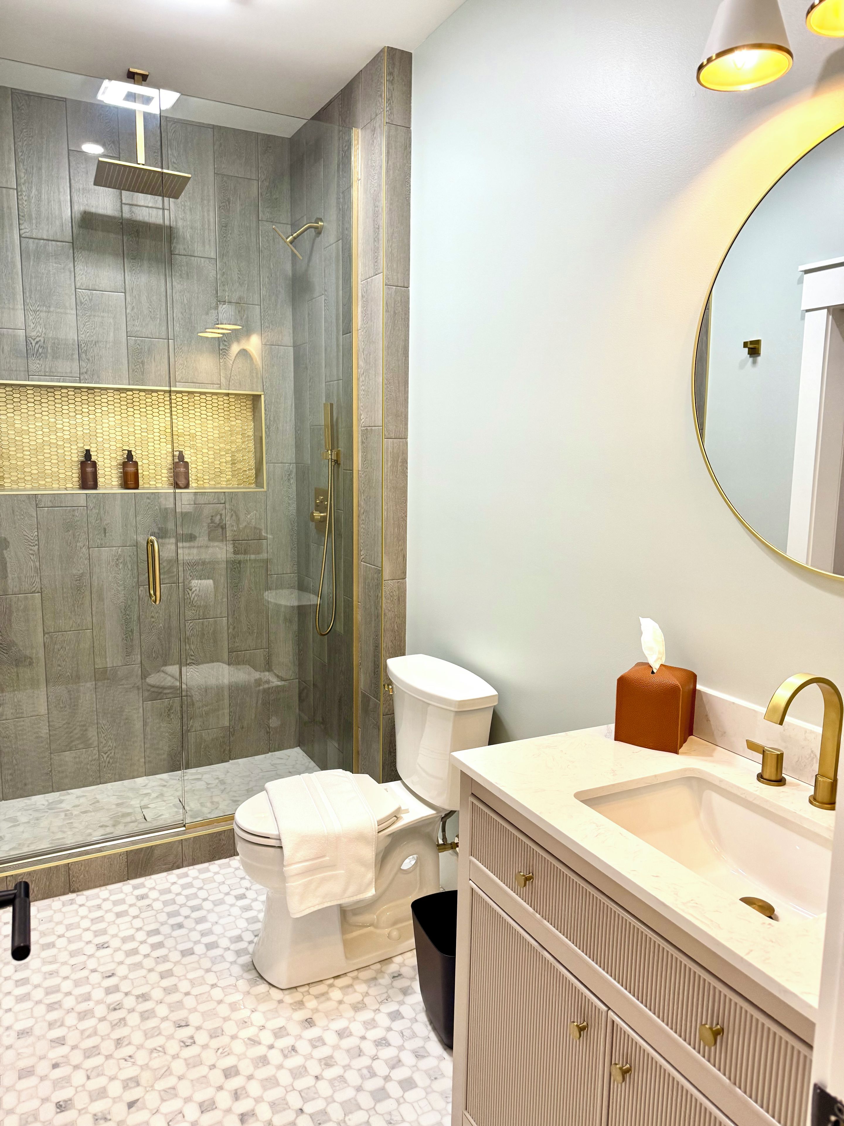 Une salle de bain moderne avec une douche à parois de verre, des toilettes, un lavabo doté d’un robinet doré et un miroir avec un cadre doré.
