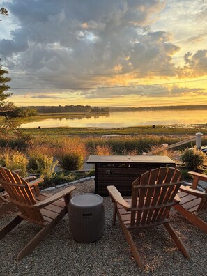 A patio with Adirondack chairs and a fire pit overlooking a body of water. - Oceanfront Stay on Plum Island Sound (Ipswich)