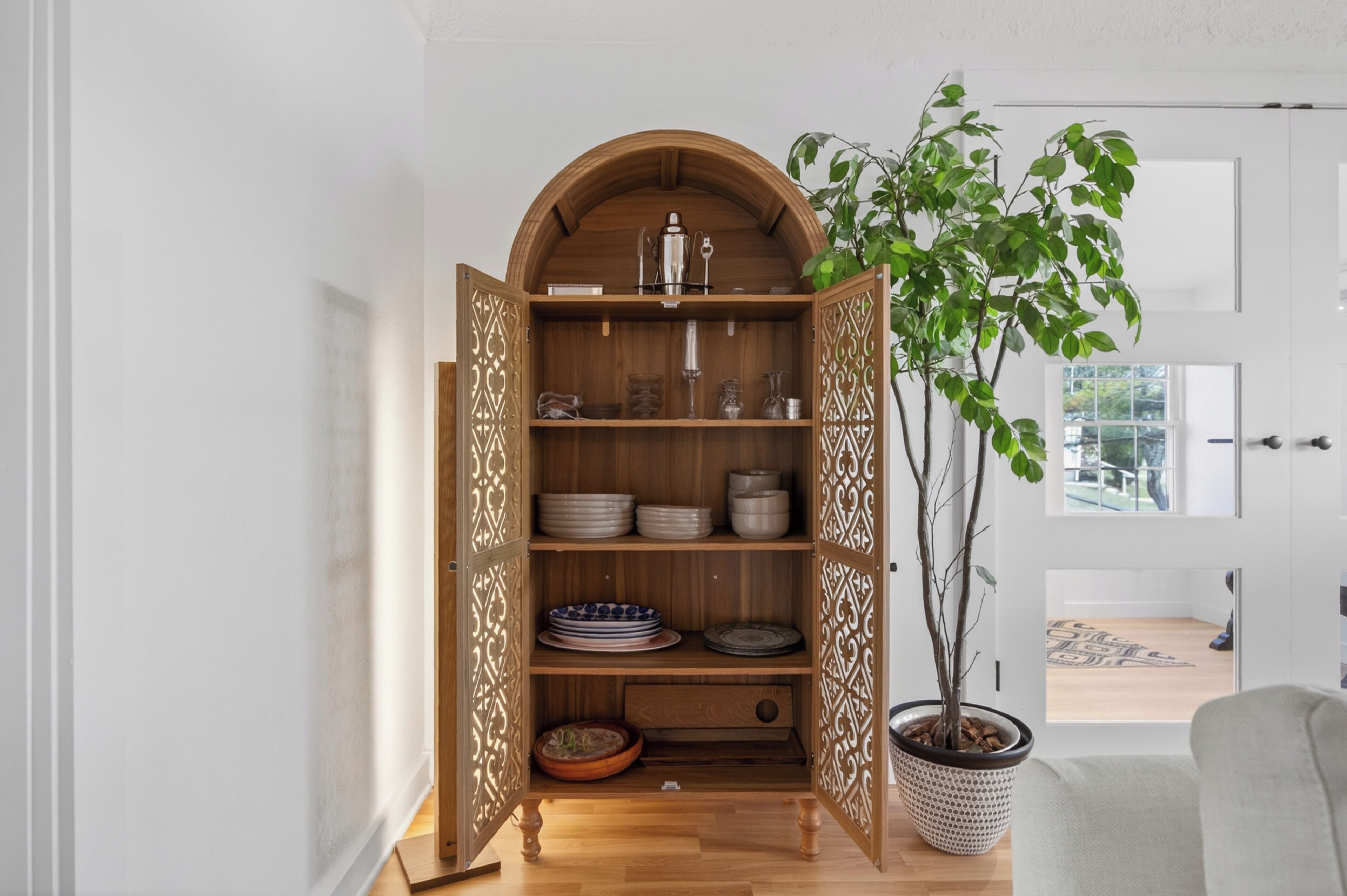 Un mueble de madera con estantes, una planta en maceta y una puerta en una habitación con una puerta blanca y una ventana.