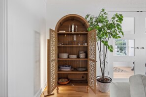 Ein Holzkabinent mit Regalen, einer Topfpflanze und einer Tür in einem Raum mit weißer Tür und Fenster.