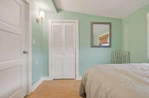 A bedroom with a bed, a white door, a closet with louvered doors, and a mirror on the wall. - Oceanfront Stay on Plum Island Sound (Ipswich)