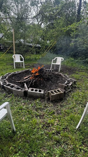 A circular concrete fire pit with two white plastic chairs on either side, surrounded by grass and trees. - Relaxing 3-bedroom Retreat W/Big Private backyard (Warren)