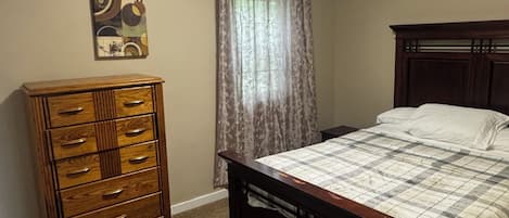 A bedroom with a bed, a dresser, a ceiling light, and a window with curtains.
