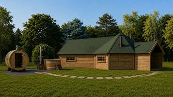 A wooden cabin with a green roof, a sauna, and a large barrel in a grassy area.