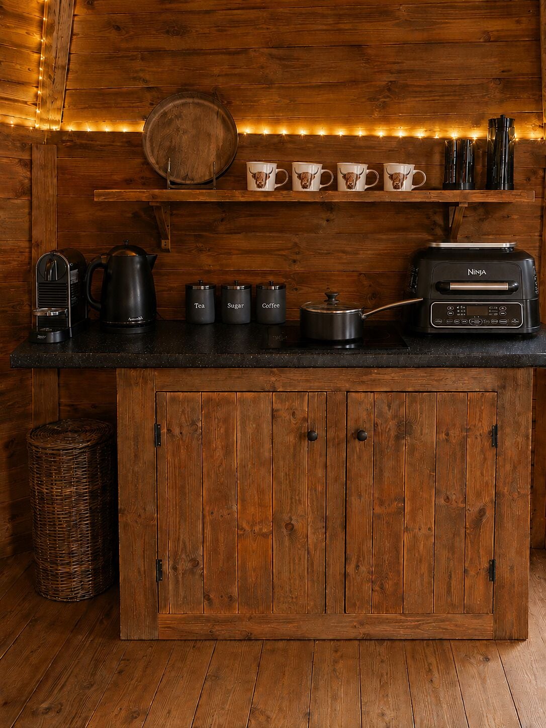 Un comptoir de cuisine en bois, avec une machine à café, des récipients à thé et à sucre, un four grille-pain de la marque Ninja et un panier.