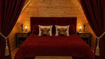A cozy bedroom with a wooden ceiling, red curtains, and a bed with two pillows featuring a bull design.