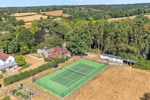 An aerial view of a residential area with a tennis court, houses, and surrounding greenery. - Tea Hut | By My Getaways (Lewes)