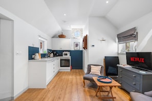 A compact living space with a kitchenette, a dining area, a seating area with a television, and a window with a view. - Tea Hut | By My Getaways (Lewes)
