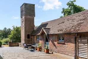 A brick building with a chimney, a small porch with a bench, and a cobblestone patio. - Tea Hut | By My Getaways (Lewes)