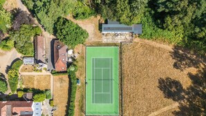 Luchtbeeld van een woonwijk met een tennisbaan, huizen en omliggend groen.
