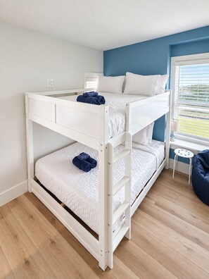 Quarto com beliche, janela, uma mesinha e um pufe azul.