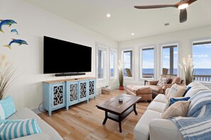 Uma sala de estar com uma TV de tela plana grande, uma mesa de centro de madeira e um sofá.