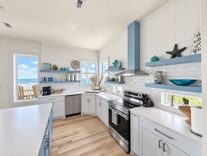 A modern kitchen with white cabinetry, a large island, and a view of the ocean. - Sunrise Chateau I Beachfront Vacation Home (Bolivar Peninsula)