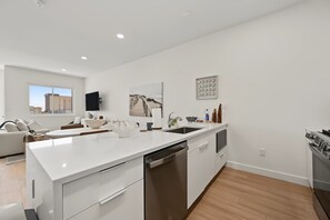 A modern kitchen with a white countertop, stainless steel appliances, and a view of the city. - The Modern East | Rooftop & Garage (Atlantic City)
