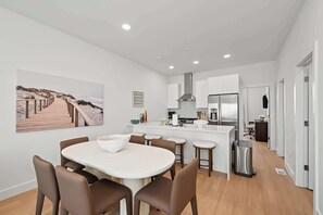 A modern kitchen with white cabinets, a stainless steel range hood, and a central island with stools. - The Modern East | Rooftop & Garage (Atlantic City)