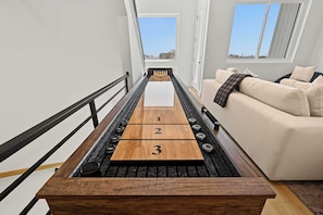 Ein schmales Brettspieltisch mit nummerierten Feldern, ein schwarzer Geländer und ein beiges Sofa in einem Raum mit weißen Wänden und Fenstern.