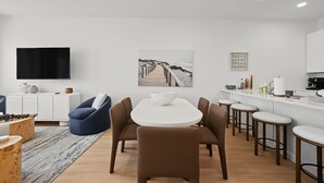 A modern kitchen with white cabinets, a flat-screen TV, a dining area with a round table and chairs, and a kitchen island with stools. - Modern Loop Retreat Duo - 2 Rooftops & 2 Garages (Atlantic City)