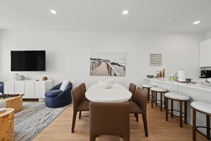 Eine moderne Küche mit weißen Schränken, einem Flachbildfernseher, einem Essbereich mit rundem Tisch und Stühlen sowie einer Kücheninsel mit Barhocker.