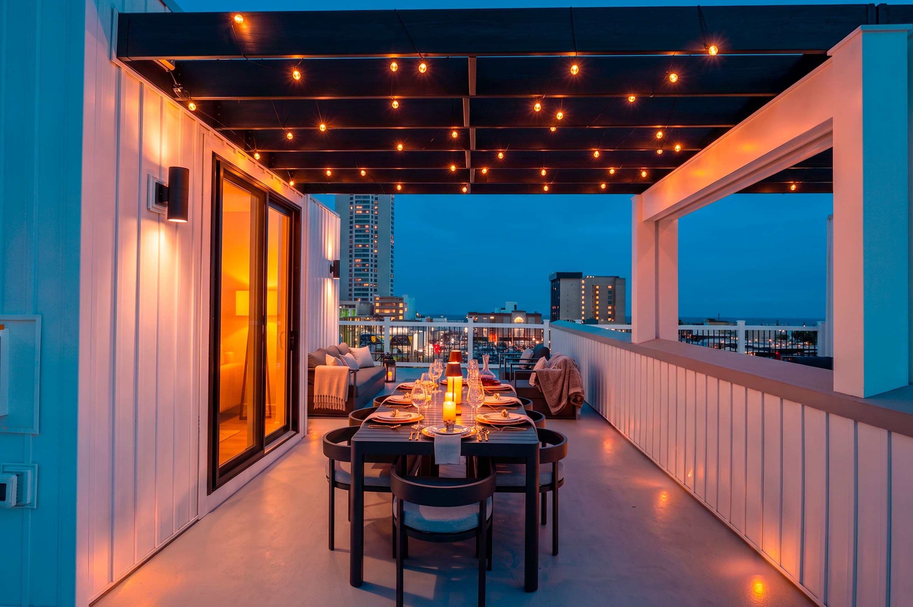 An outdoor dining area with a table set for two, overlooking a cityscape at dusk.
