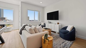 A modern living room with a sofa, a blue armchair, a coffee table, and a TV mounted on the wall. - Modern Loop Retreat Duo - 2 Rooftops & 2 Garages (Atlantic City)
