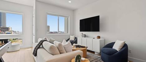 Un salon moderne avec un canapé, un fauteuil bleu, une table basse et un téléviseur fixé au mur.