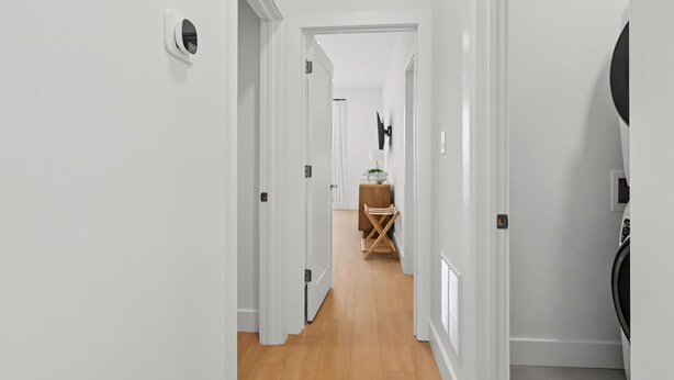 A hallway with white walls, a wooden floor, and a door leading to a room with a bed and a TV. - Modern Loop Retreat Duo - 2 Rooftops & 2 Garages (Atlantic City)